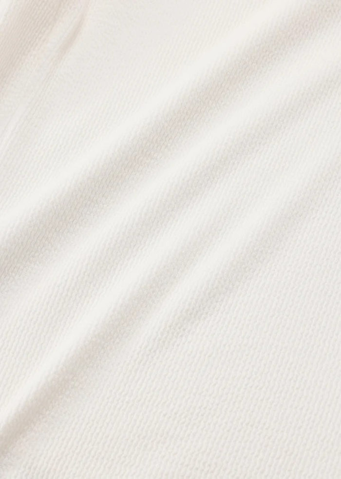 A close-up of a soft, off-white or cream-colored fabric with a fine ribbed texture and gentle diagonal folds.